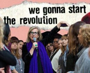 An image of Vickie Saundersin a blue scarf holding a microphone surrounded by women, text behind her reads "we are gonna start the revolution"