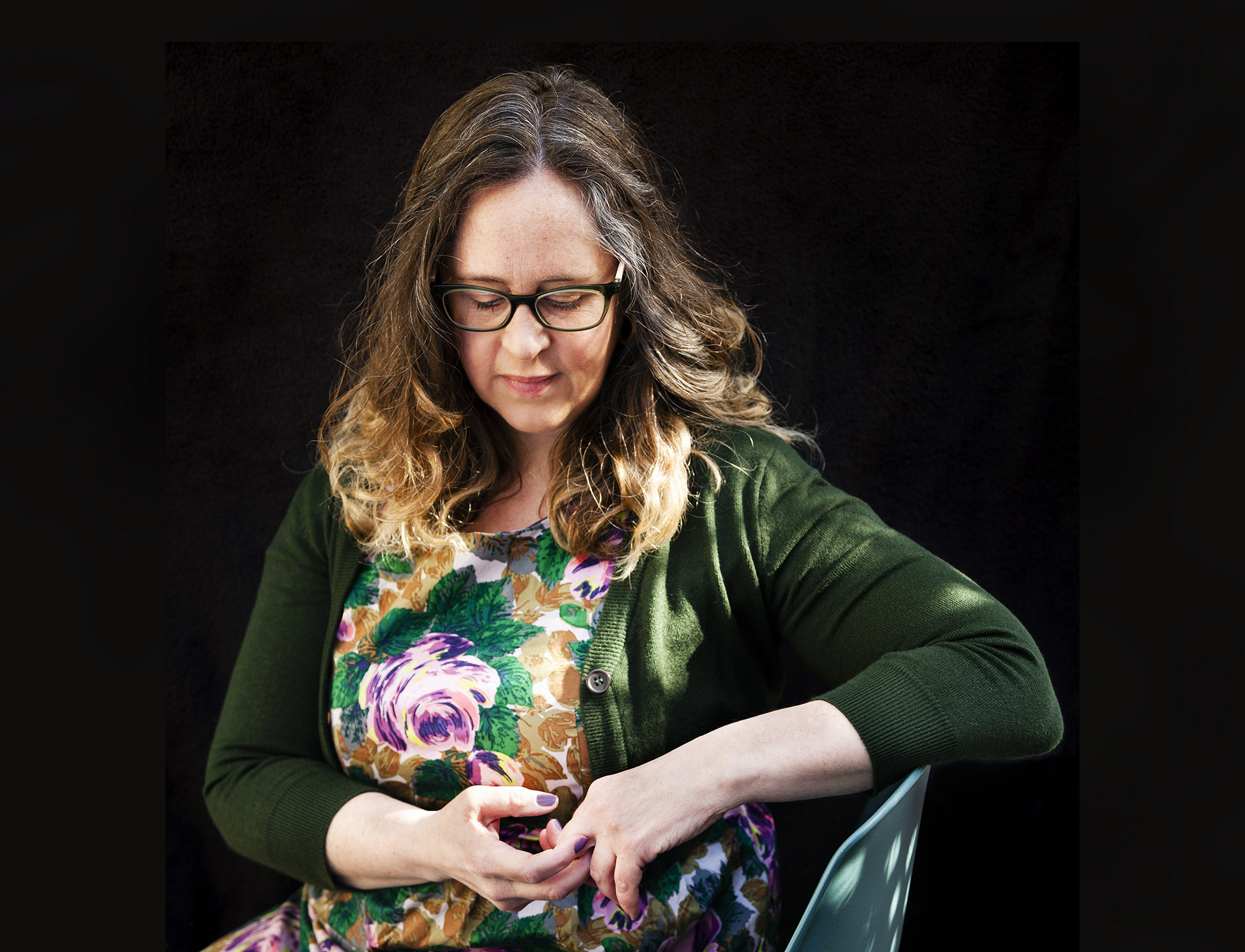 Photo of artist Jennifer Long sitting on a chair looking at her hands.