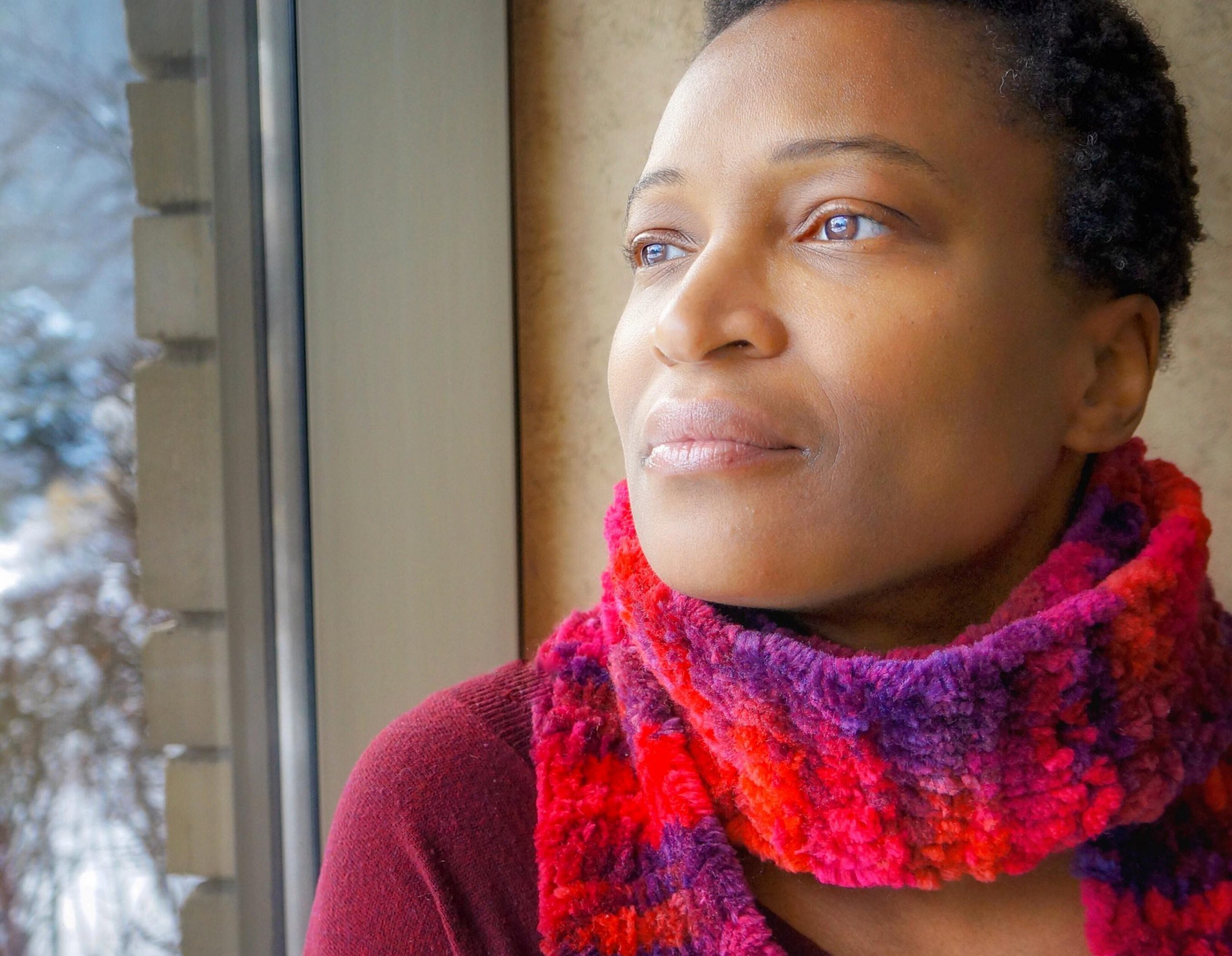 A Black woman wearing a red scarf entrepreneur gazing outside a window.