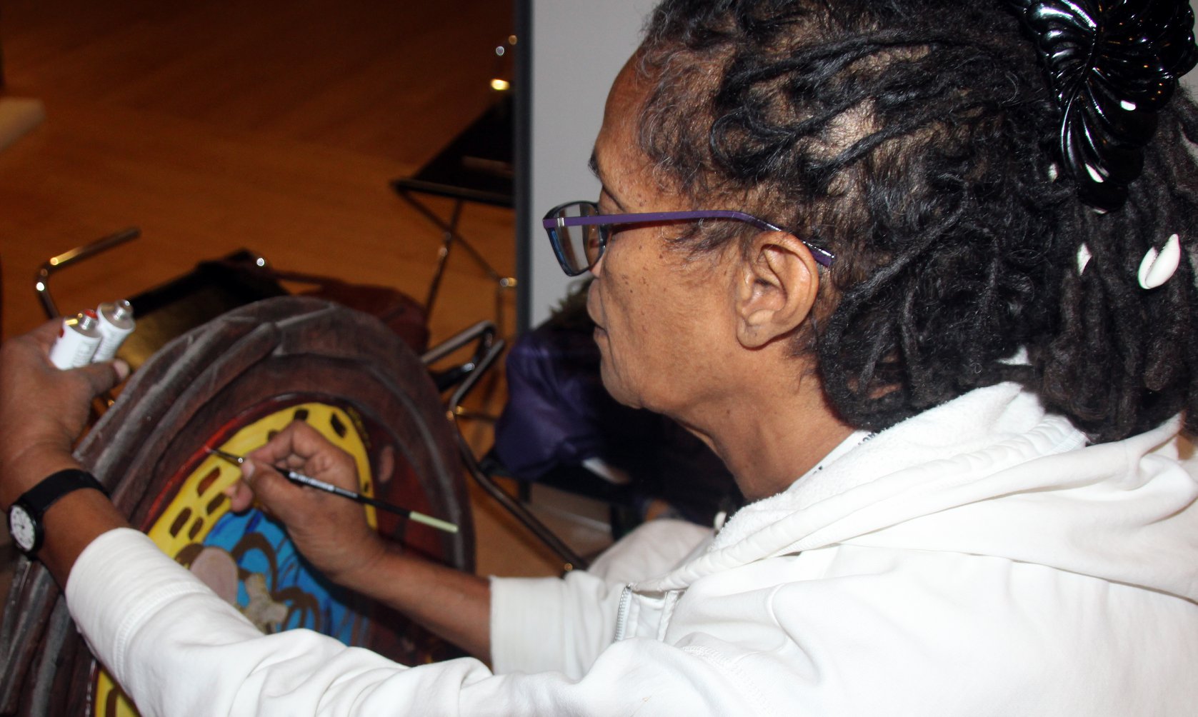 A photo of a black woman artist, Winsom Winsom, in a white short, learning forwrard, painting