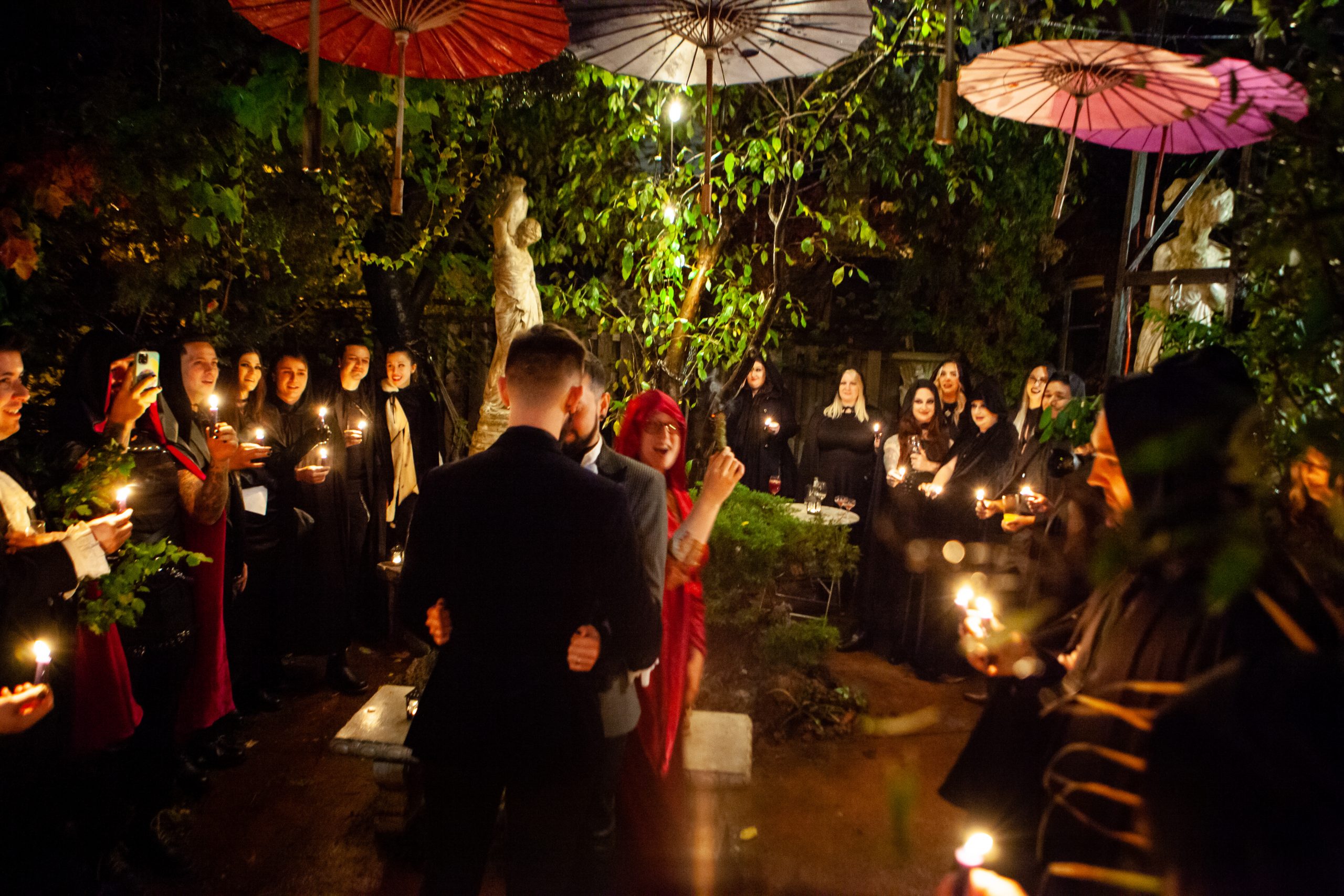 Small group of people holding candles standing around two men who are cerimoniously being blessed by Annie Matan