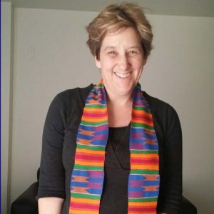 Image of woman with brown hair, black top and multi-colored scarf sitting