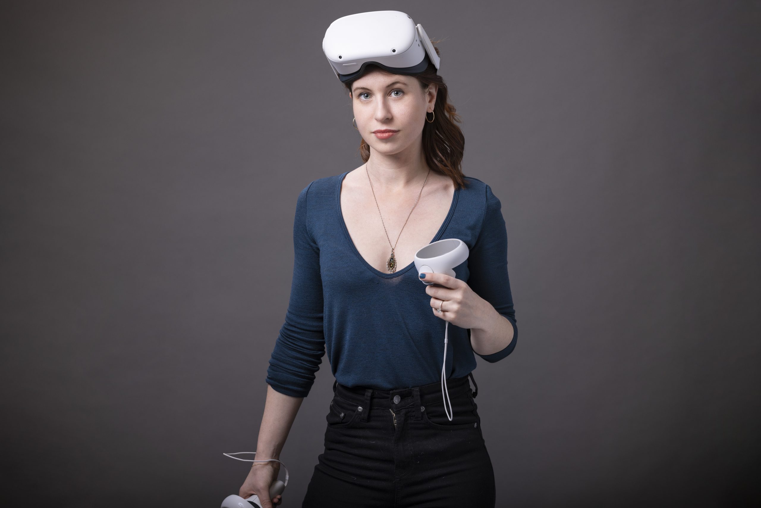 Photo of a young woman wearing a blue v neck sweater and a virtual reality headset.