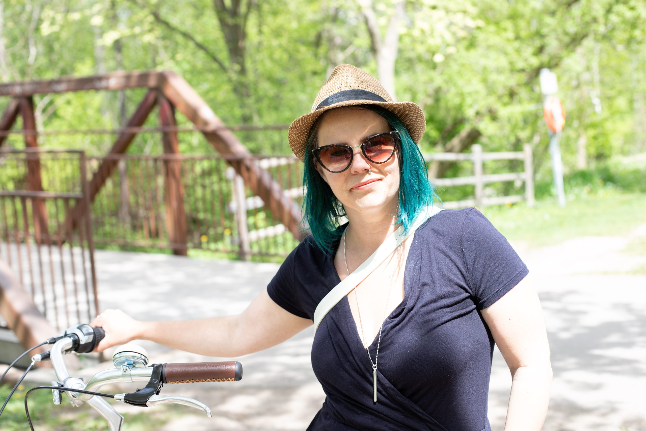 Photo of middle aged woman with turquoise, mid lenght hair wearing a hat, riding a bike on a sunny day.